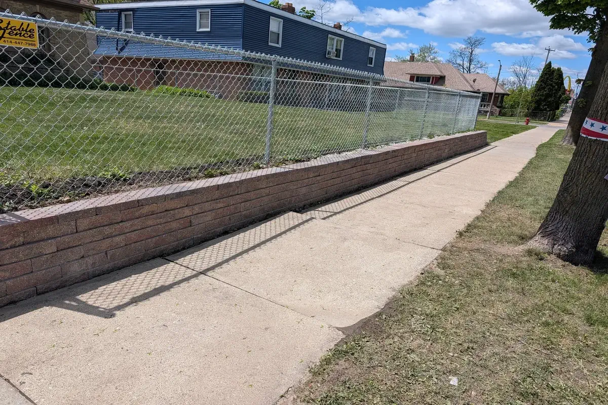 Chainlink fence anchored on a low block wall beside a Milwaukee sidewalk