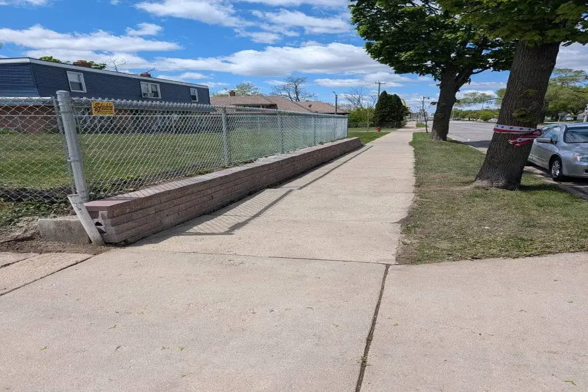 Block retaining wall carrying a chainlink fence along a public sidewalk