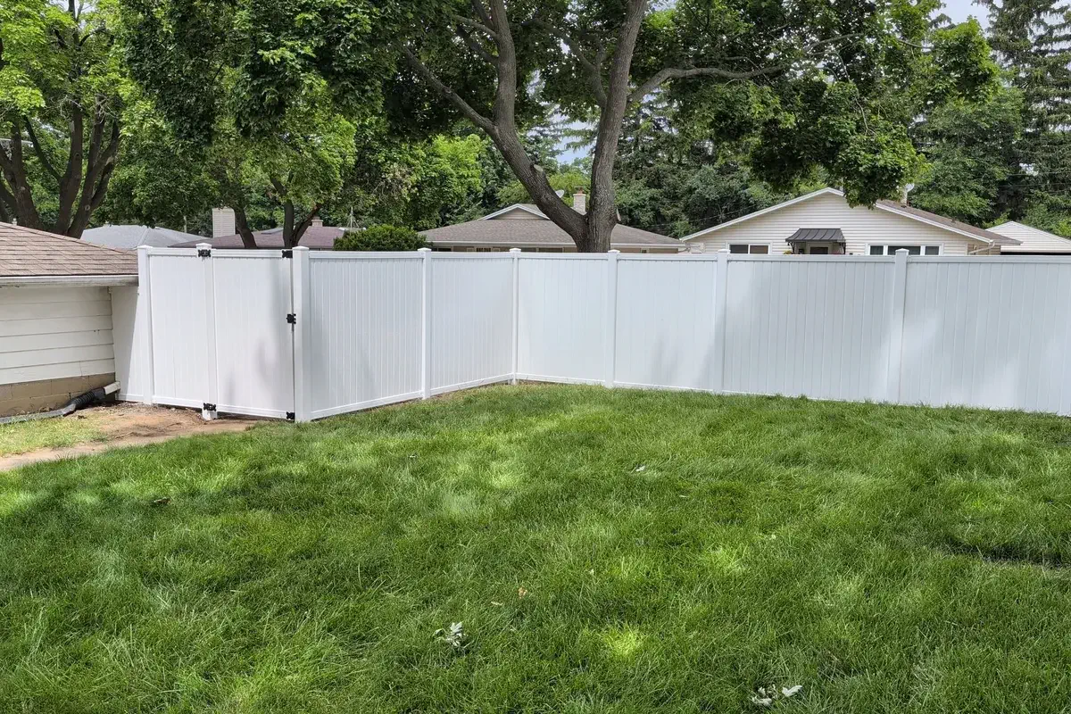 White vinyl fence wrapping a shaded backyard