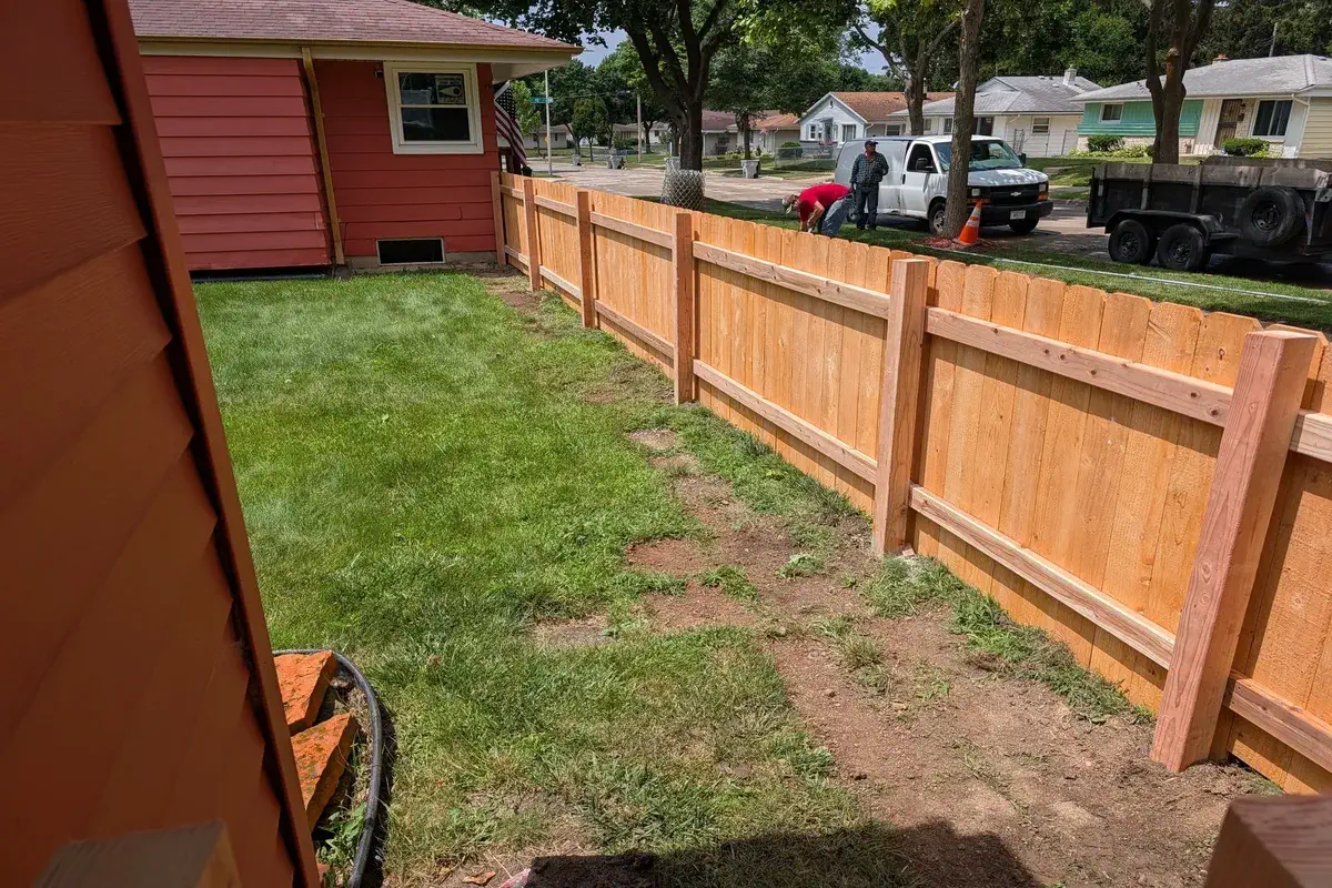 Wood privacy fence running the length of a side yard beside a red house