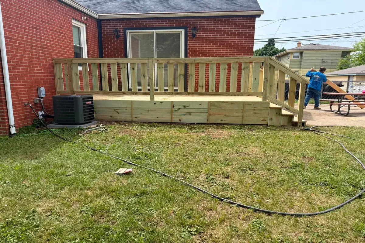 Raised wood deck with railing finished behind a brick home